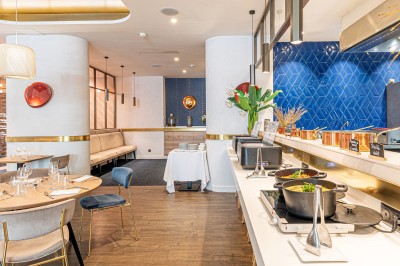 Buffet de petit-déjeuner avec viennoiseries, pain, fruits et fontaine de chocolat dans une salle décorée de motifs tropicaux.