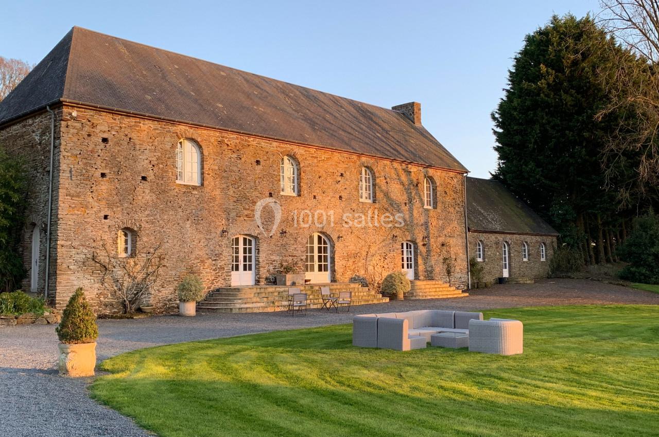 Façade d'une maison en pierre avec toit en ardoise, entourée d'une pelouse et de mobilier d'extérieur.