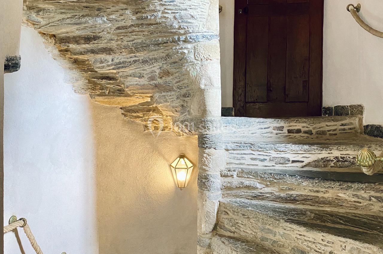Escalier en pierre en colimaçon avec des murs blancs, une rampe en corde et une porte en bois en haut.