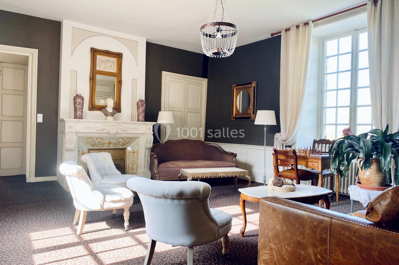 Salon lumineux avec cheminée décorative, mobilier classique, lustre en cristal et grande fenêtre laissant entrer la lumière.