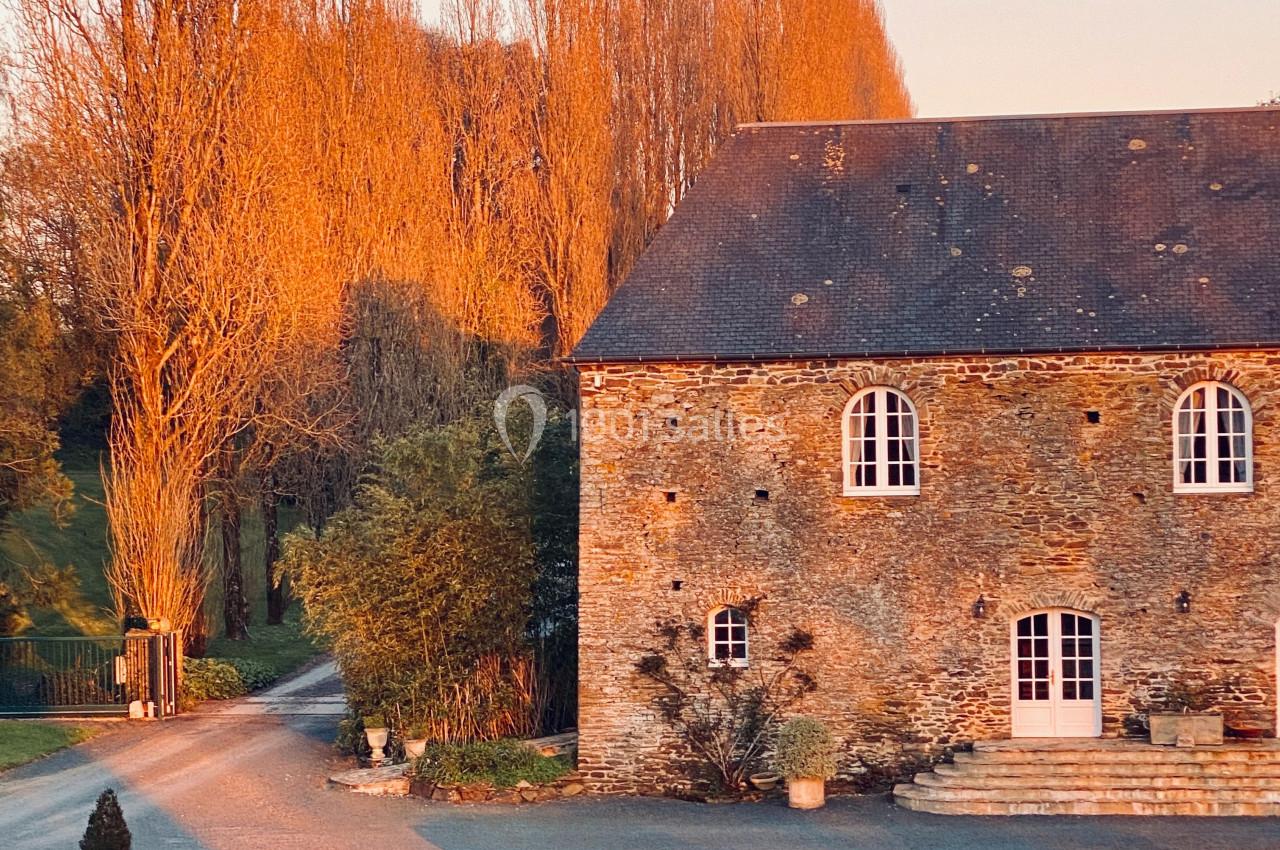 Maison en pierre éclairée par la lumière du coucher de soleil, entourée d'arbres et d'une pelouse bien entretenue.
