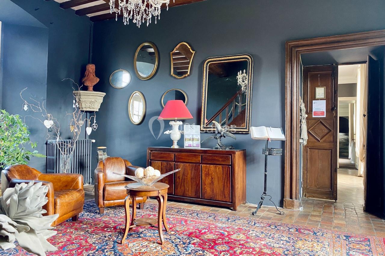 Salon élégant avec murs sombres, meubles en bois, tapis coloré, miroirs accrochés et lustre en cristal.