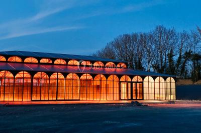 Structure en verre illuminée par des lumières violettes au crépuscule, avec un ciel dégagé en arrière-plan.