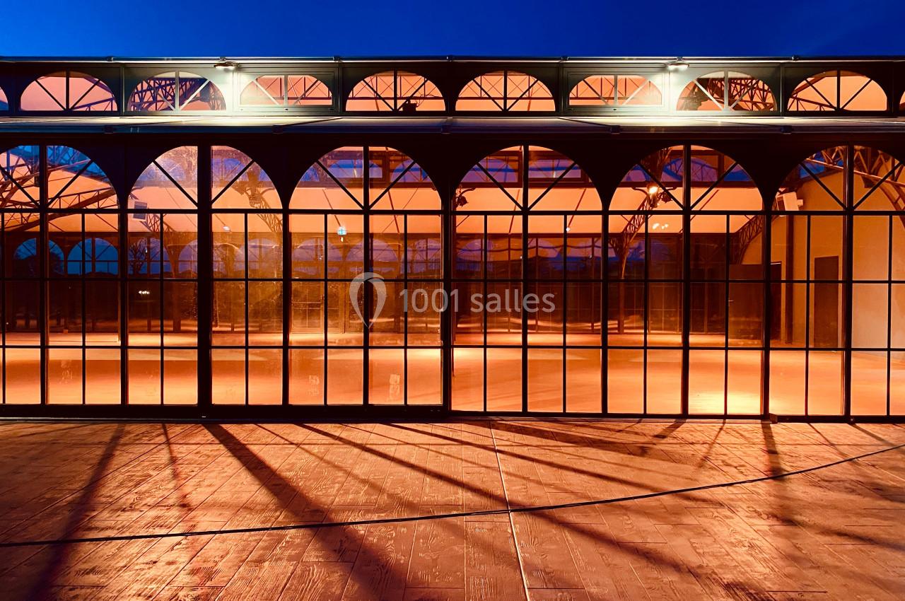 Grande verrière illuminée à la tombée de la nuit, reflétant des teintes orangées sur un sol en bois.