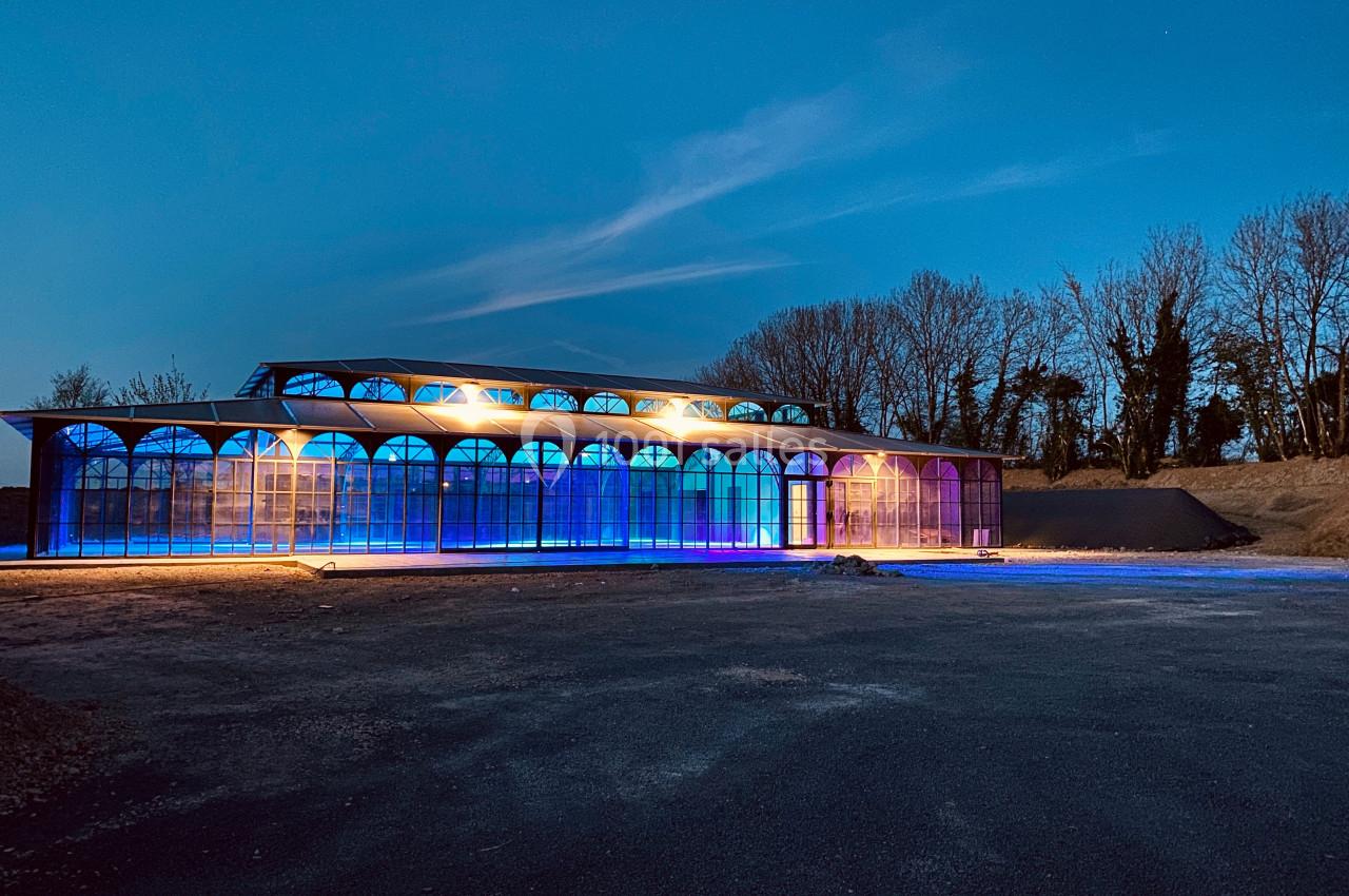 Bâtiment vitré illuminé par des lumières colorées dans un paysage nocturne avec des arbres en arrière-plan.
