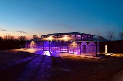 Structure en verre illuminée par des lumières violettes au crépuscule, avec un ciel dégagé en arrière-plan.
