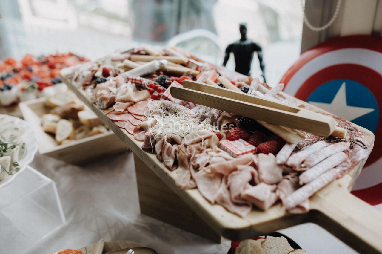 Plateau en bois garni de charcuteries, fromages, fruits rouges et germes, présenté sur une table de réception.