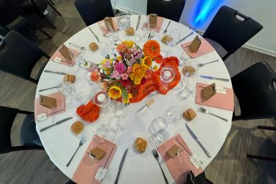 Centre de table avec bougies torsadées, fleurs colorées et nappe orange, entouré de verres et couverts.