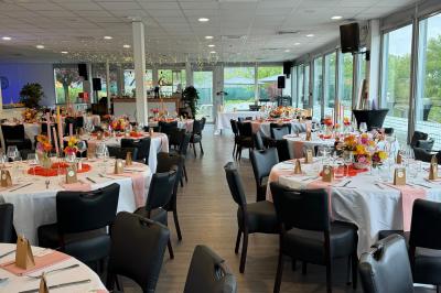 Centre de table avec bougies torsadées, fleurs colorées et nappe orange, entouré de verres et couverts.