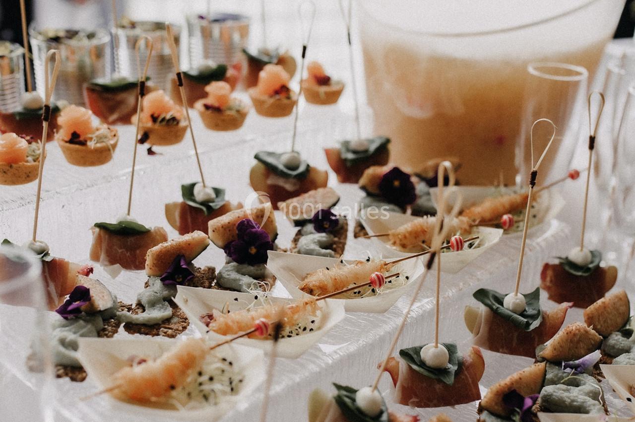 Plateau de bouchées apéritives variées avec brochettes, verrines et décorations florales sur une table.