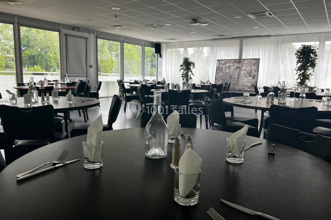Salle de restaurant lumineuse avec tables dressées, grandes baies vitrées donnant sur un espace extérieur verdoyant.