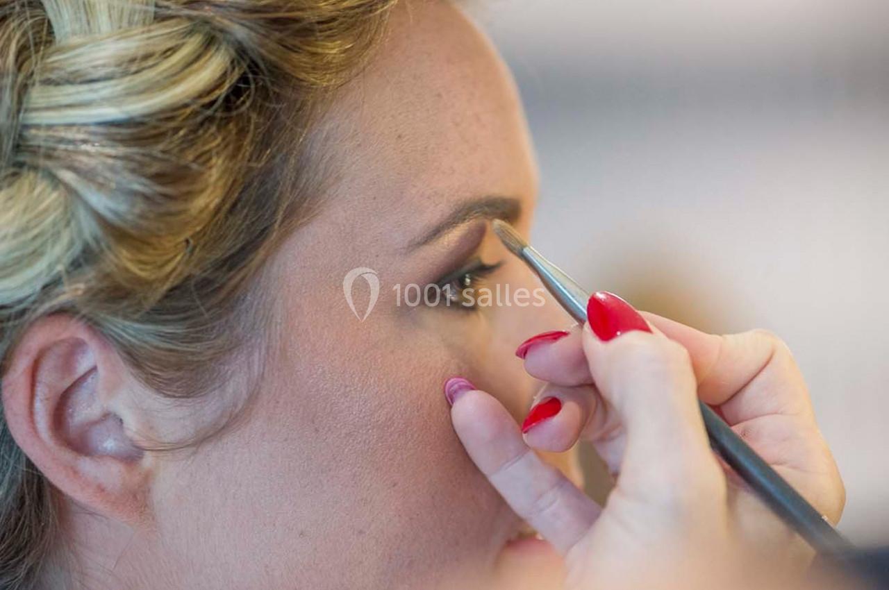 Une personne applique du maquillage sur les sourcils d'une femme aux cheveux blonds coiffés.