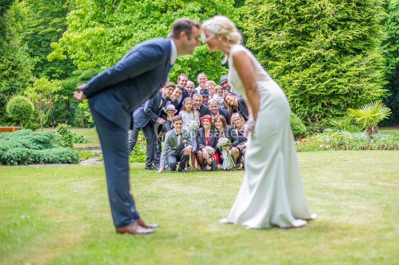 Un couple en tenue de mariage s'incline face à face sur une pelouse, entouré d'invités souriants en arrière-plan.