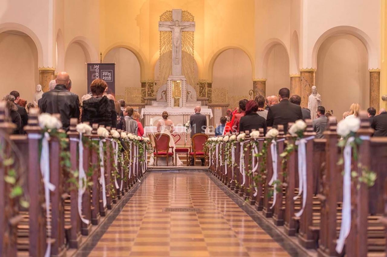 Des personnes assistent à une cérémonie religieuse dans une église décorée de fleurs blanches.