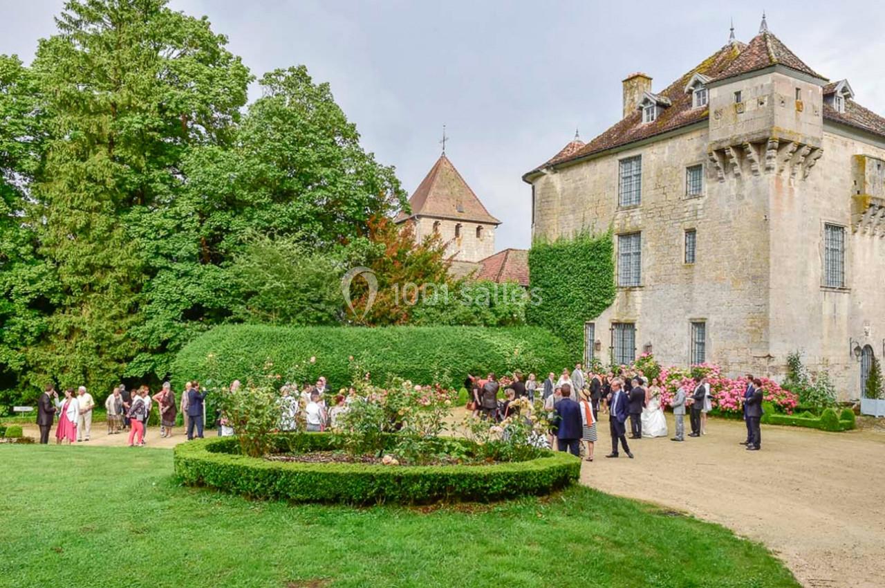 Groupe de personnes rassemblées dans un jardin devant un château entouré de verdure et de rosiers.