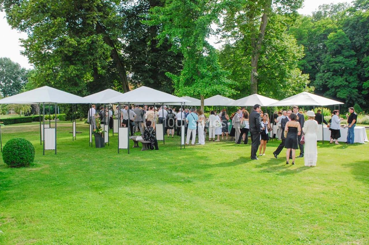 Groupe de personnes rassemblées sous des tonnelles blanches dans un jardin verdoyant par une journée ensoleillée.