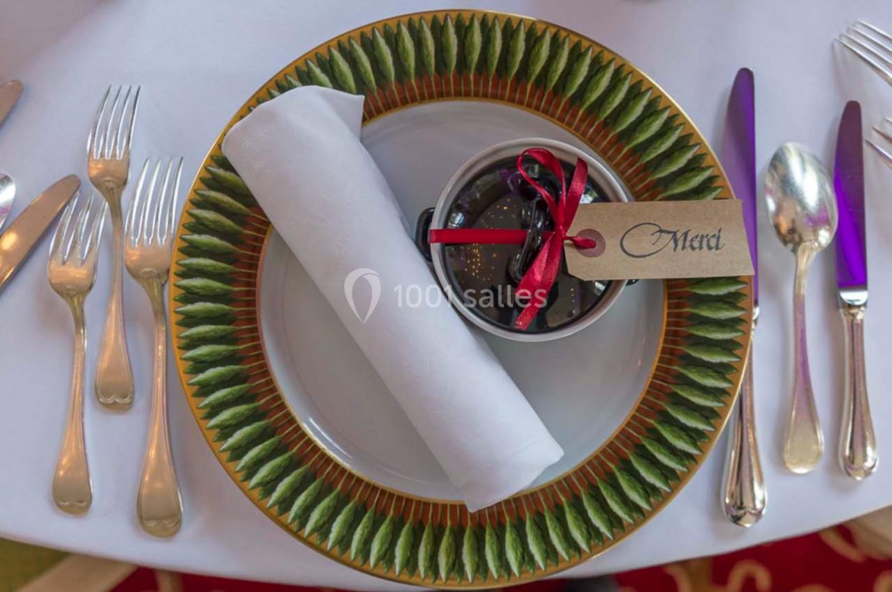 Assiette décorative avec serviette blanche roulée et petit pot cadeau avec étiquette ’Merci’, entourée de couverts.