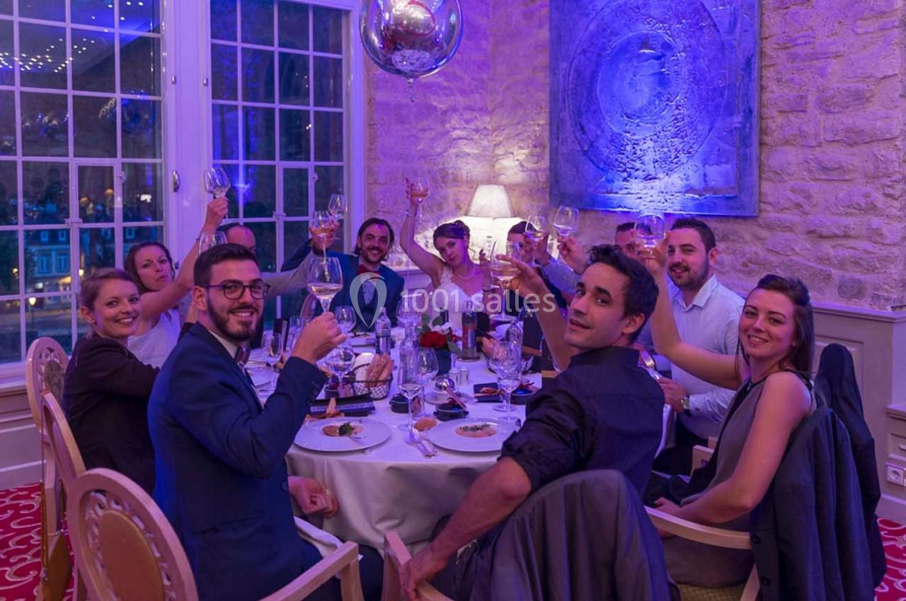 Un groupe de personnes souriantes trinque autour d'une table dressée dans une salle élégante avec un mur en pierre.