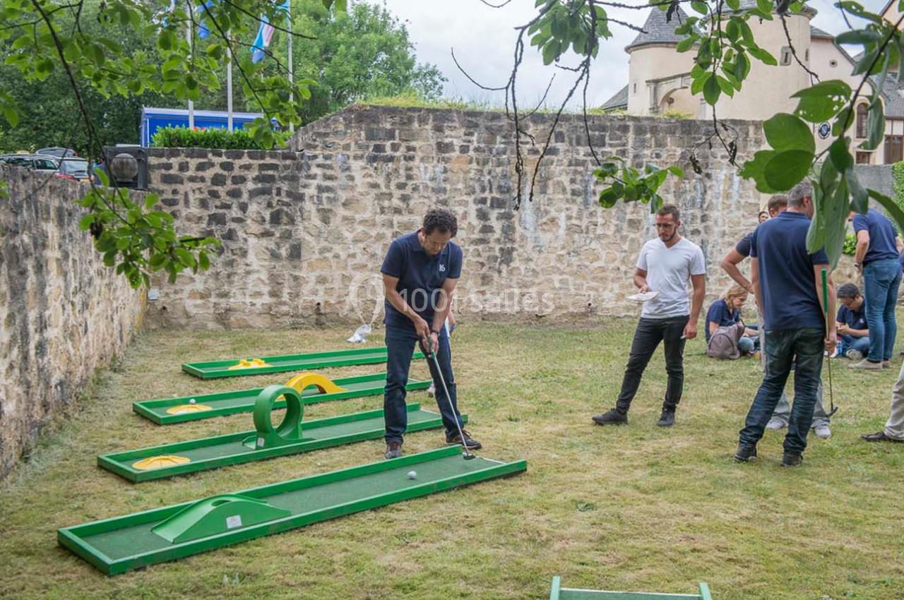 Un homme joue au mini-golf sur une pelouse avec des obstacles, entouré de plusieurs personnes.