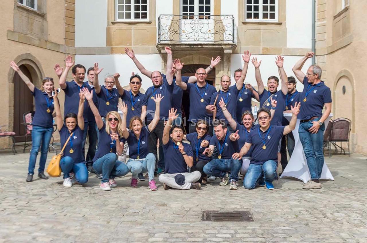 Un groupe de personnes en polos bleus pose joyeusement devant un bâtiment historique avec des médailles autour du cou.