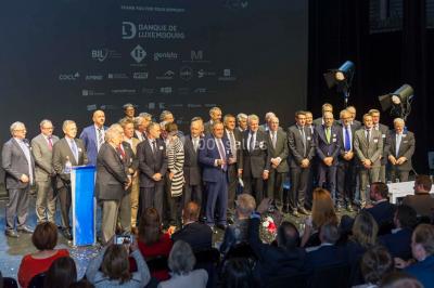 Un groupe de personnes en tenue formelle pose sur une scène lors d'un événement avec un écran affichant des logos en arrière…