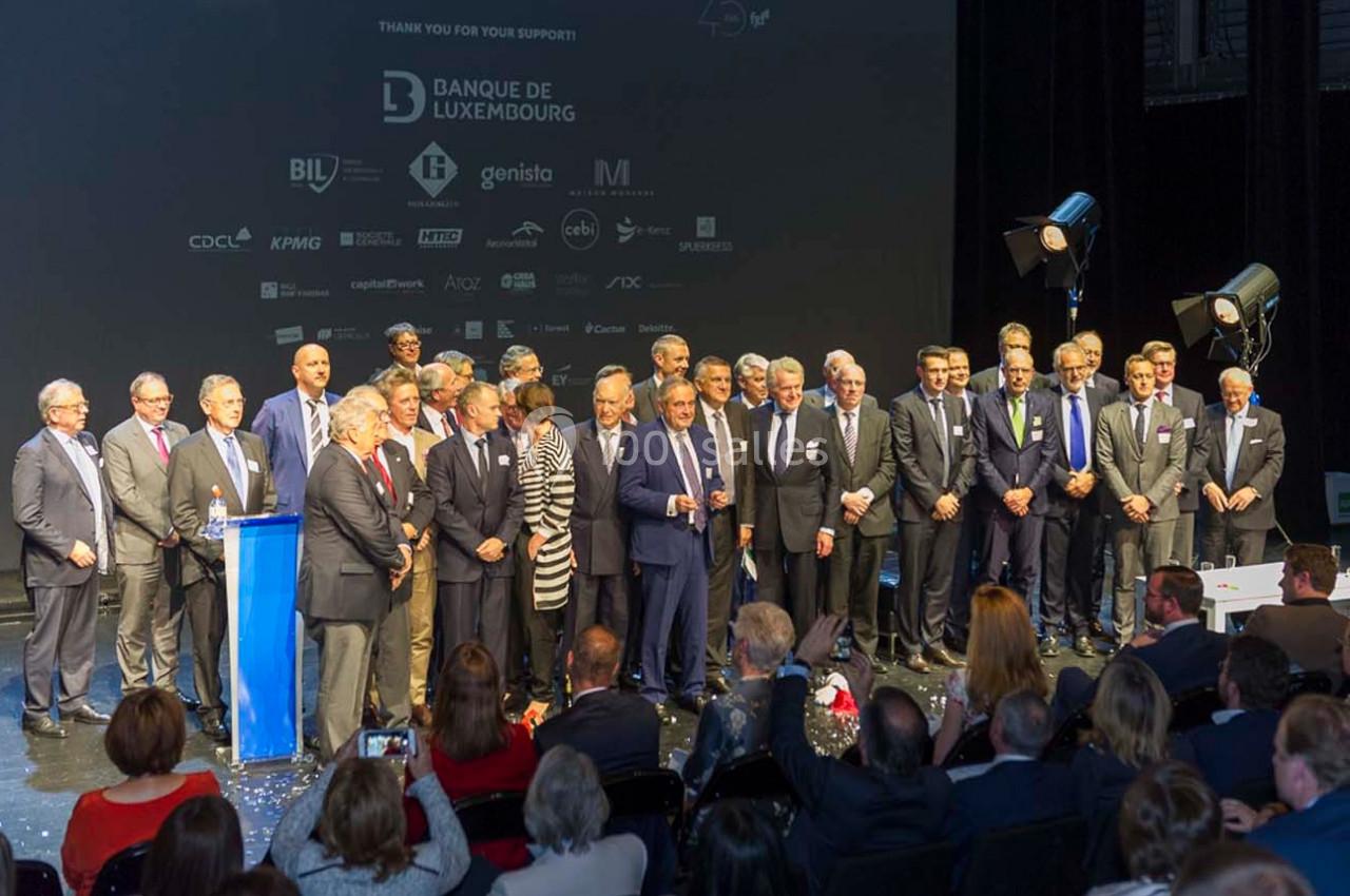 Un groupe de personnes en tenue formelle pose sur une scène lors d'un événement avec un écran affichant des logos en arrière…