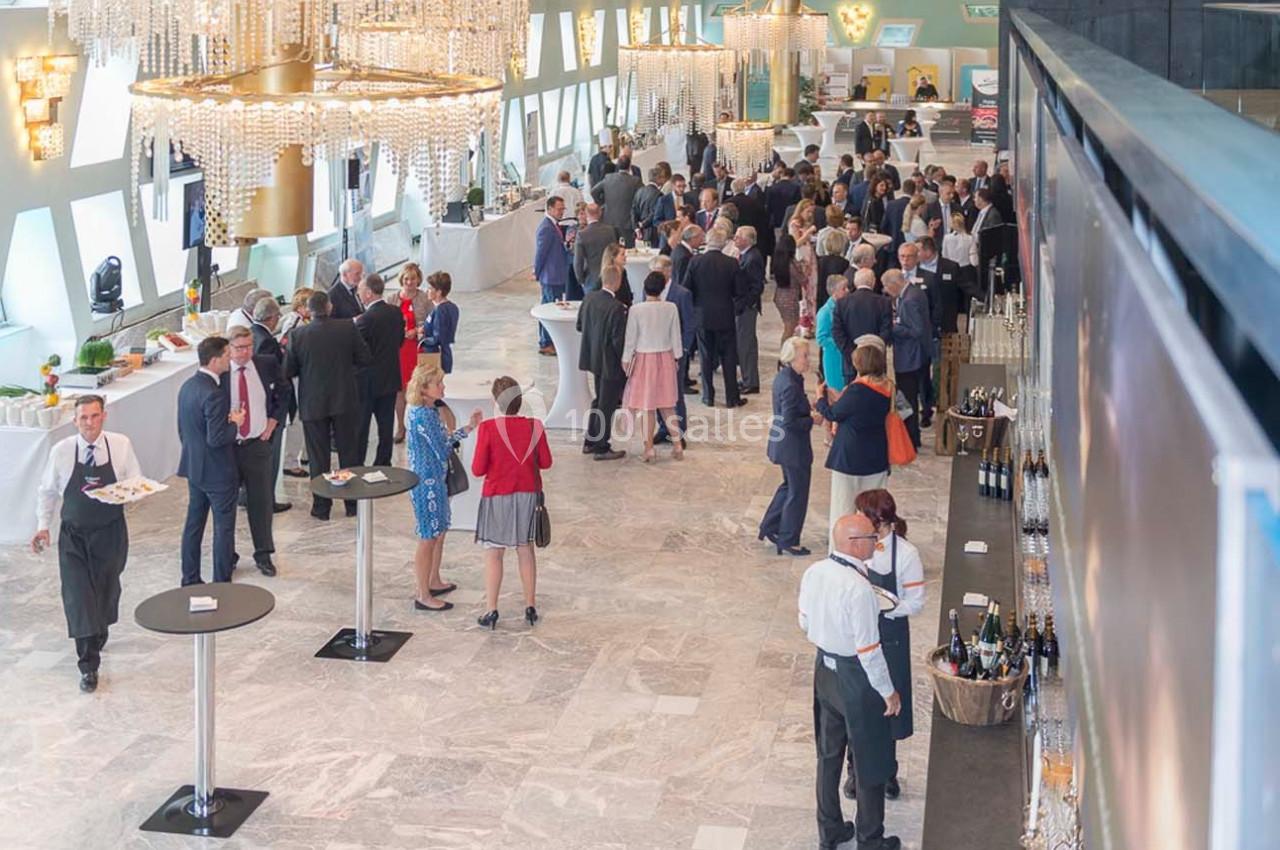 Groupe de personnes en tenue formelle discutant et se servant lors d'un événement dans une grande salle lumineuse.