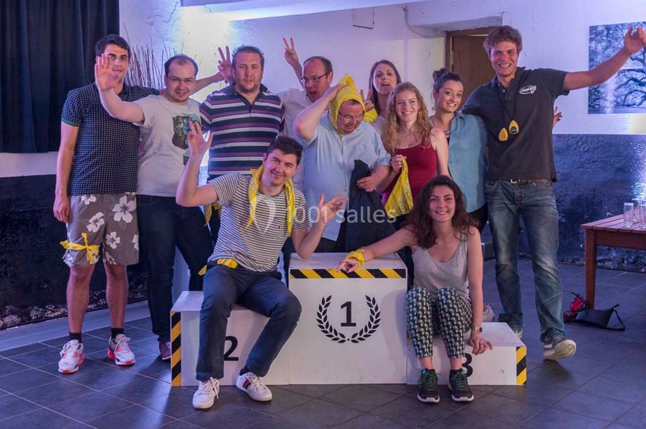 Un groupe de personnes souriantes posant autour d'un podium numéroté dans une ambiance festive en intérieur.