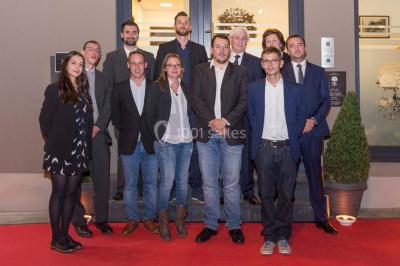 Un groupe de personnes en tenue formelle pose sur une scène lors d'un événement avec un écran affichant des logos en arrière…