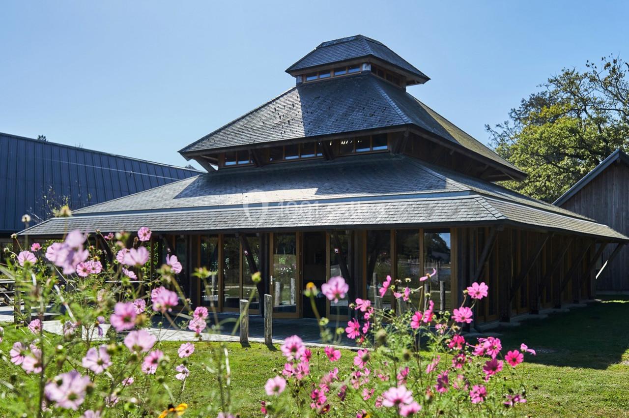 Bâtiment en bois à l'architecture moderne entouré de fleurs roses et d'un espace vert sous un ciel dégagé.