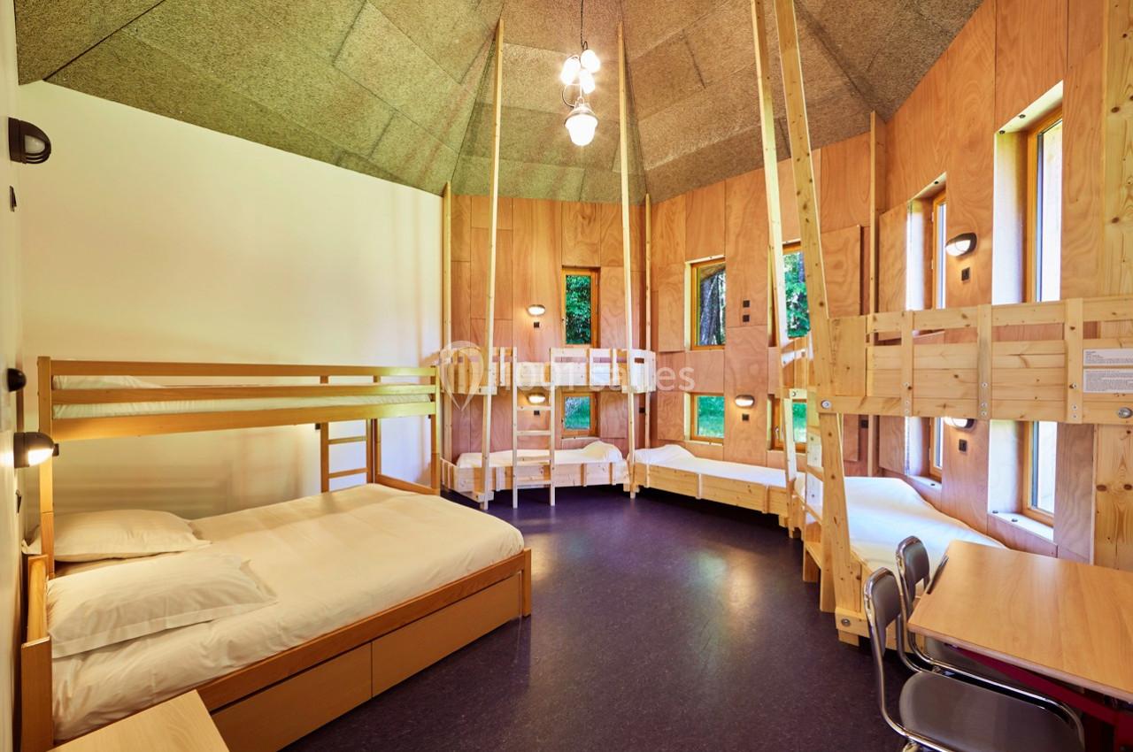 Chambre en bois avec plusieurs lits superposés, un lit double, des fenêtres et un éclairage suspendu.