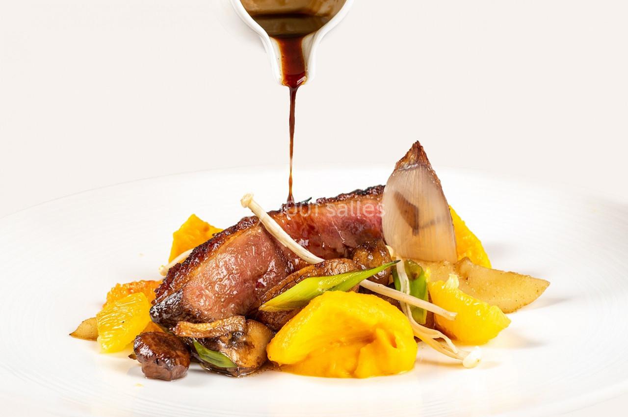 Tranche de viande servie avec légumes variés et sauce versée sur l'assiette blanche.