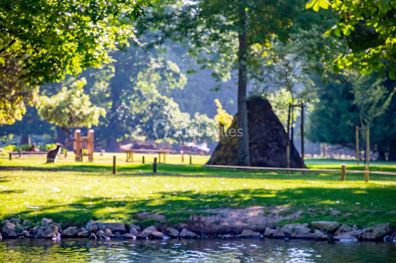 Vue d'un parc verdoyant avec des arbres, une pelouse, un plan d'eau et une structure en pierre au centre.