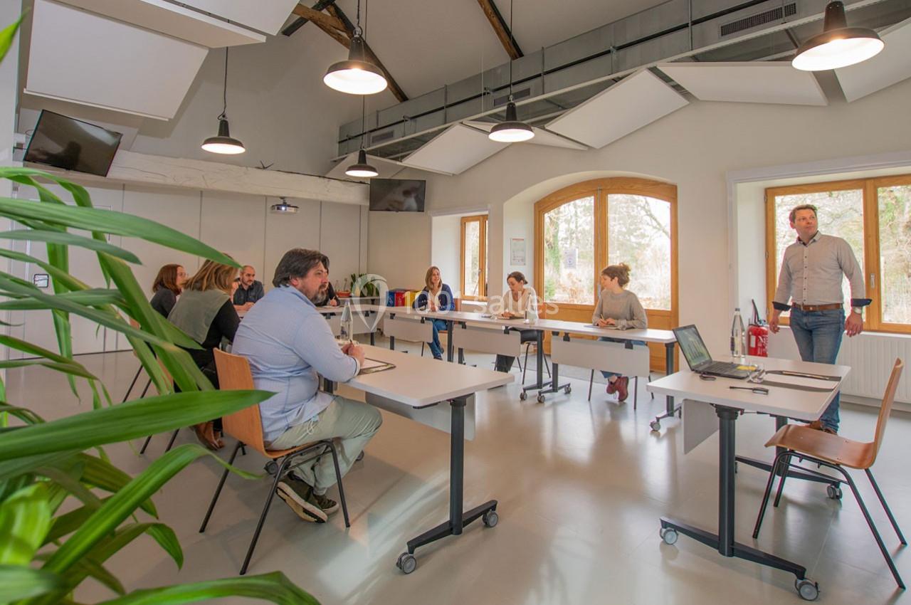 Un groupe de personnes assises autour de tables en formation, dans une salle lumineuse avec de grandes fenêtres.
