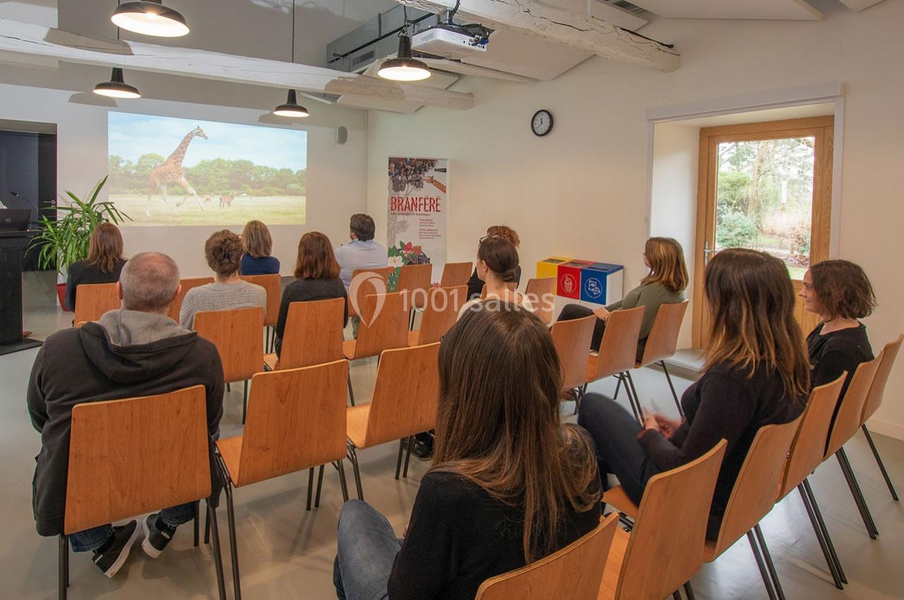 Des personnes assises dans une salle regardent une projection montrant une girafe dans un paysage naturel.