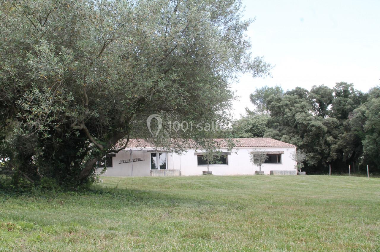 Bâtiment blanc de plain-pied entouré d'arbres, avec une pelouse au premier plan et un ciel dégagé.