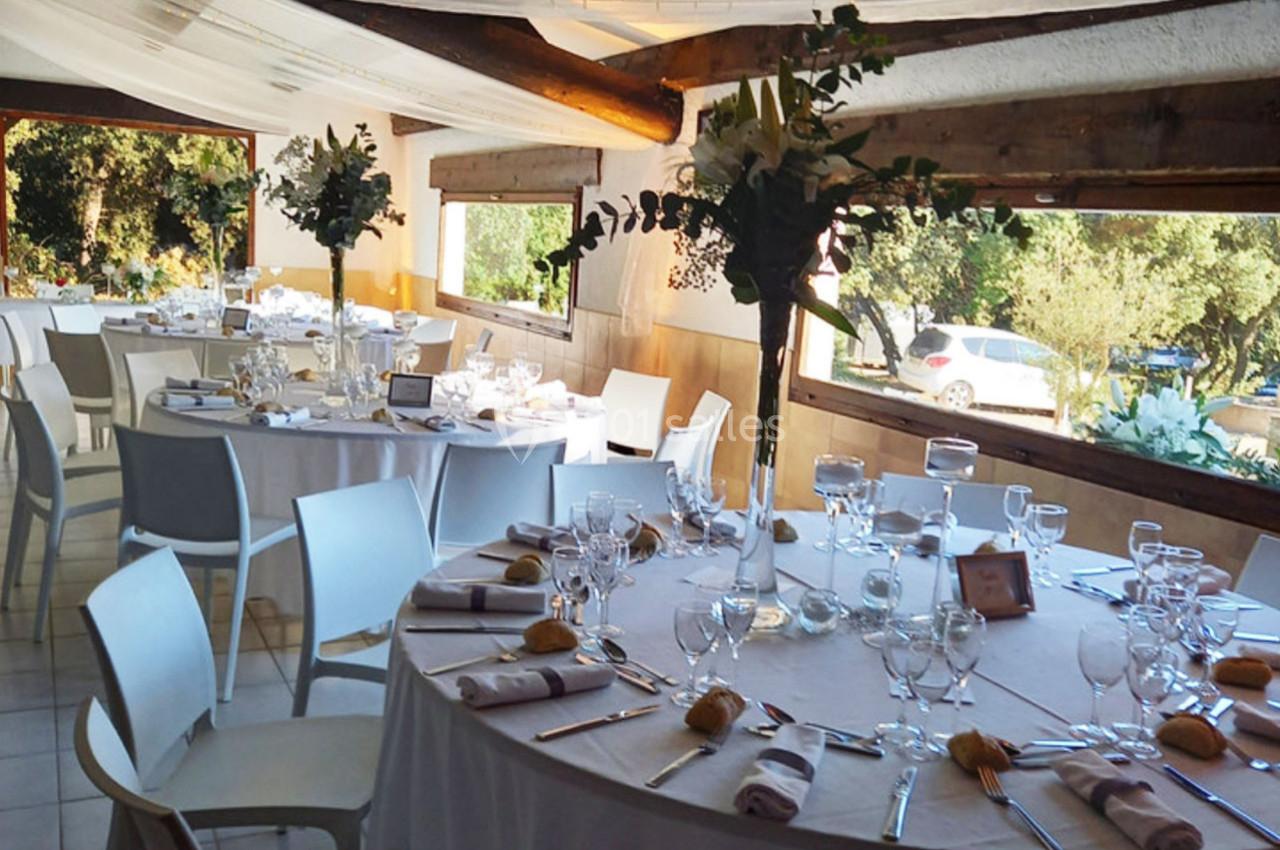 Salle de réception décorée avec des tables rondes dressées, nappes blanches, verres et compositions florales.