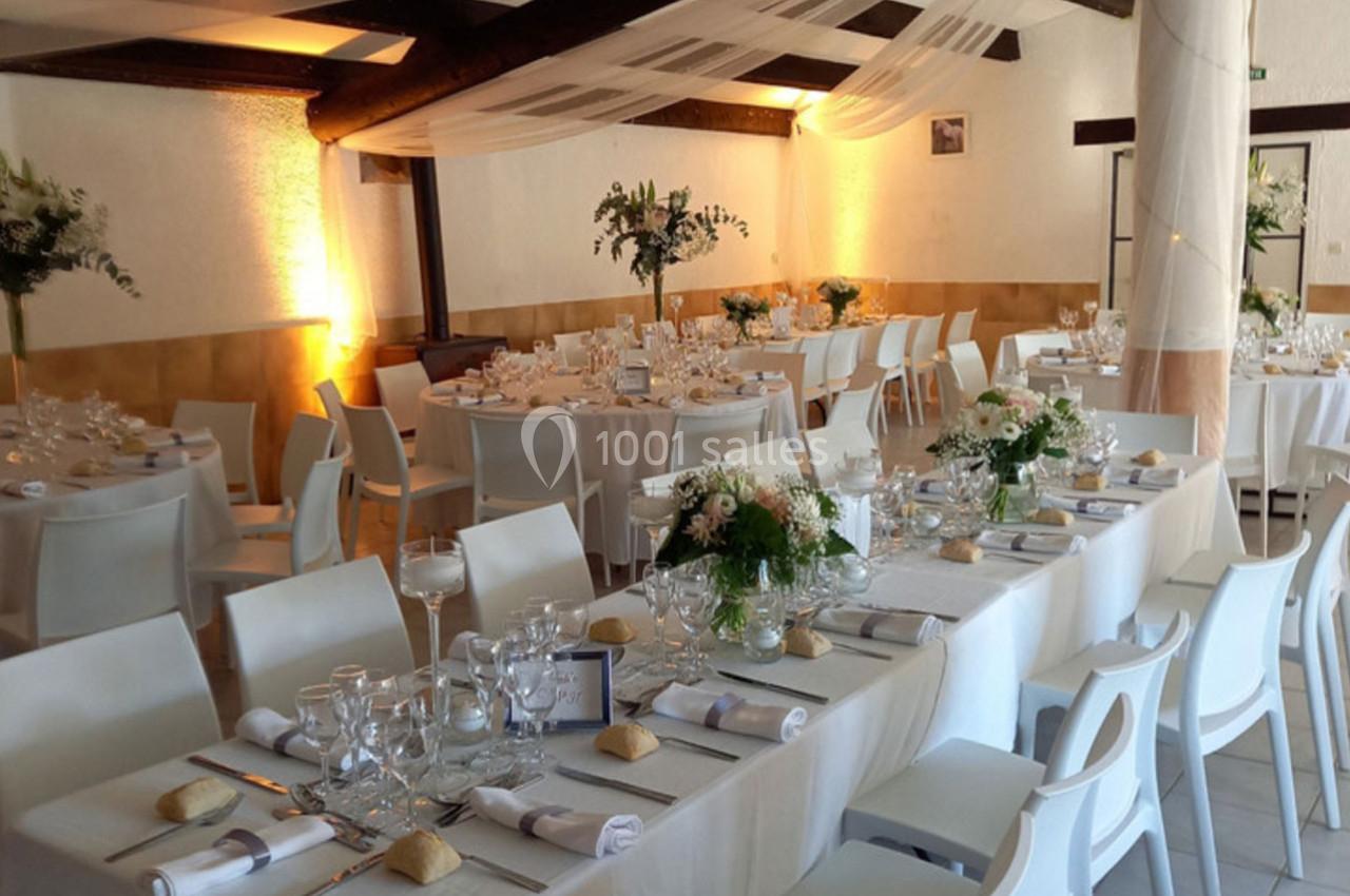 Salle de réception décorée avec des tables dressées, nappes blanches, compositions florales et éclairage chaleureux.