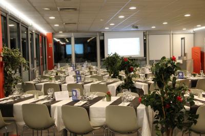 Salle de conférence lumineuse avec des participants assis, une présentation projetée et une table de buffet au premier plan.