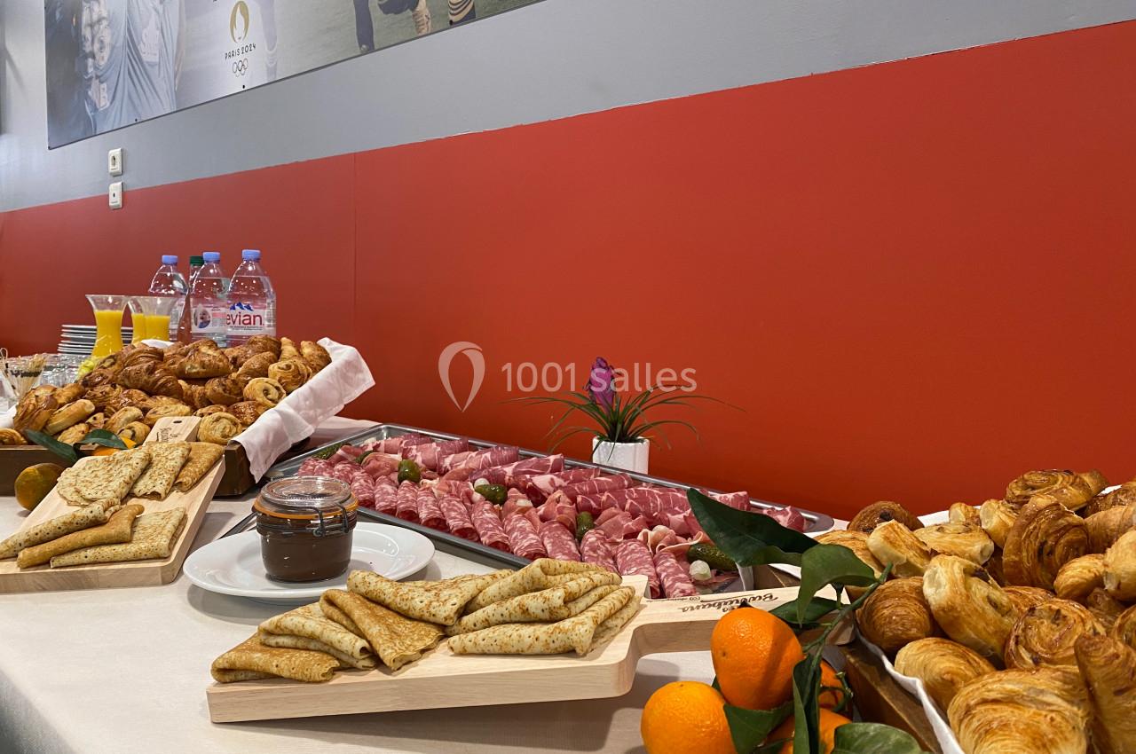 Buffet composé de crêpes, viennoiseries, charcuterie, jus de fruits et eau, disposé sur une table blanche.