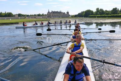 Un groupe de personnes souriantes pose dans une salle avec des rameurs et un écran projeté en arrière-plan.