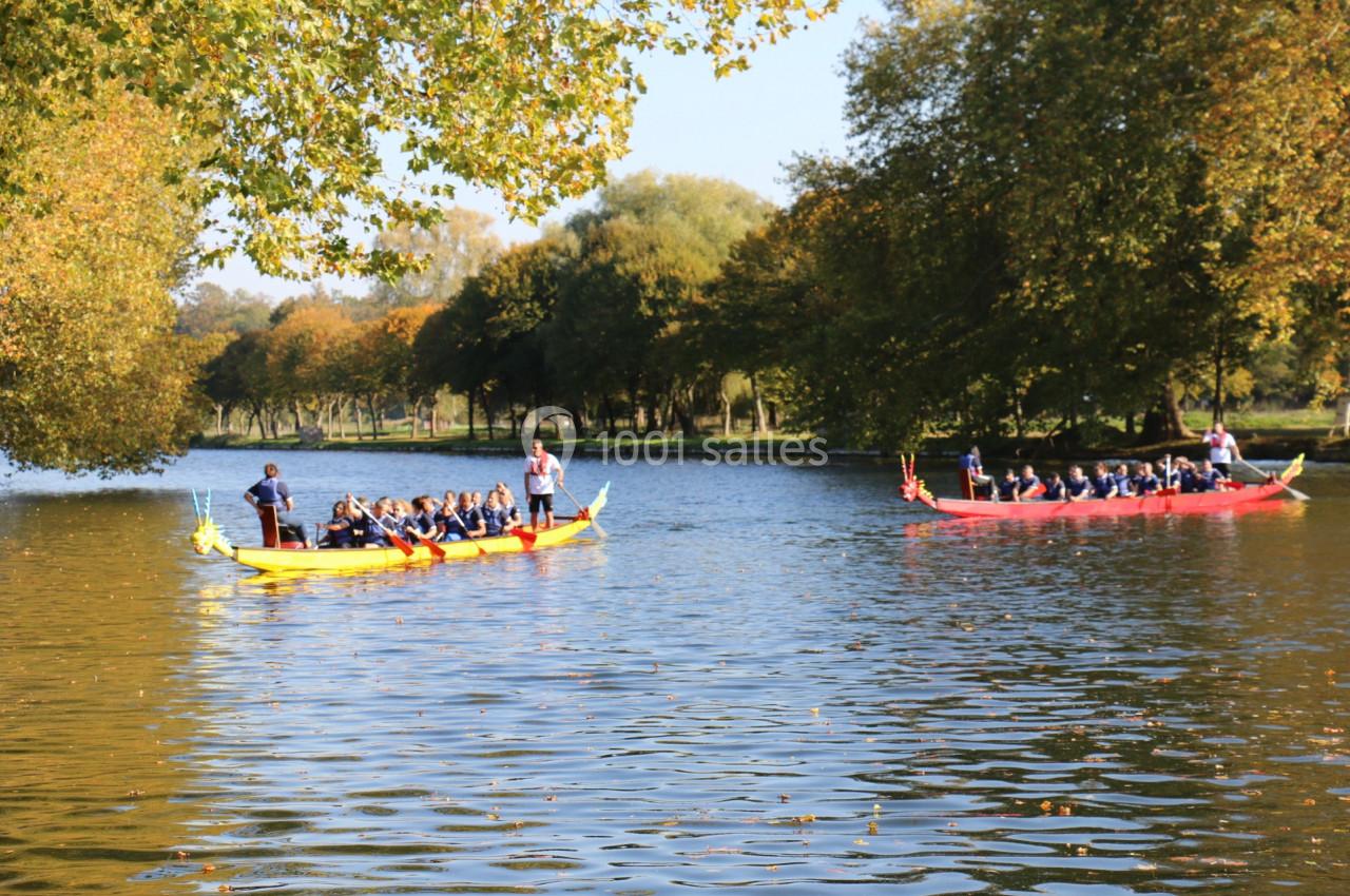 Deux barques colorées avec des passagers naviguent sur un lac entouré d'arbres en automne.