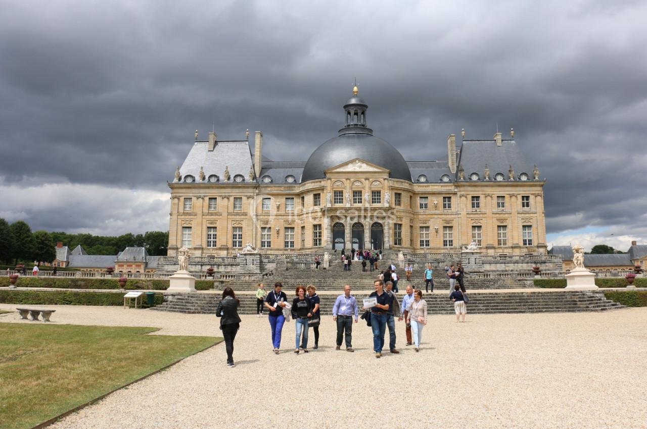 Groupe de visiteurs devant le château de Vaux-le-Vicomte sous un ciel nuageux.