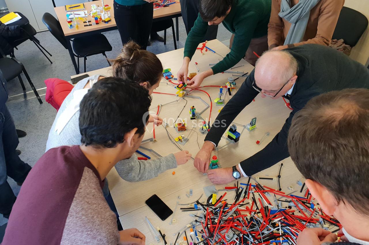 Des personnes assemblent des pièces de Lego colorées sur une table lors d'une activité collaborative en intérieur.