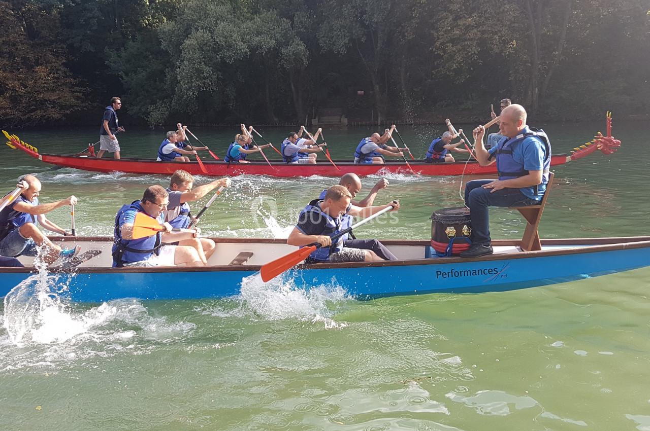 Des personnes pagaient en équipe dans deux bateaux-dragons sur un lac entouré de végétation.