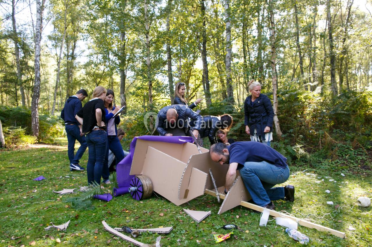 Des personnes assemblent une structure en carton dans une clairière boisée lors d'une activité de groupe.