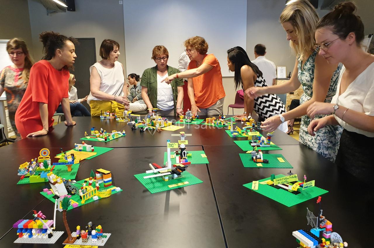 Des personnes collaborent autour de tables noires avec des constructions en Lego dans une salle de réunion.