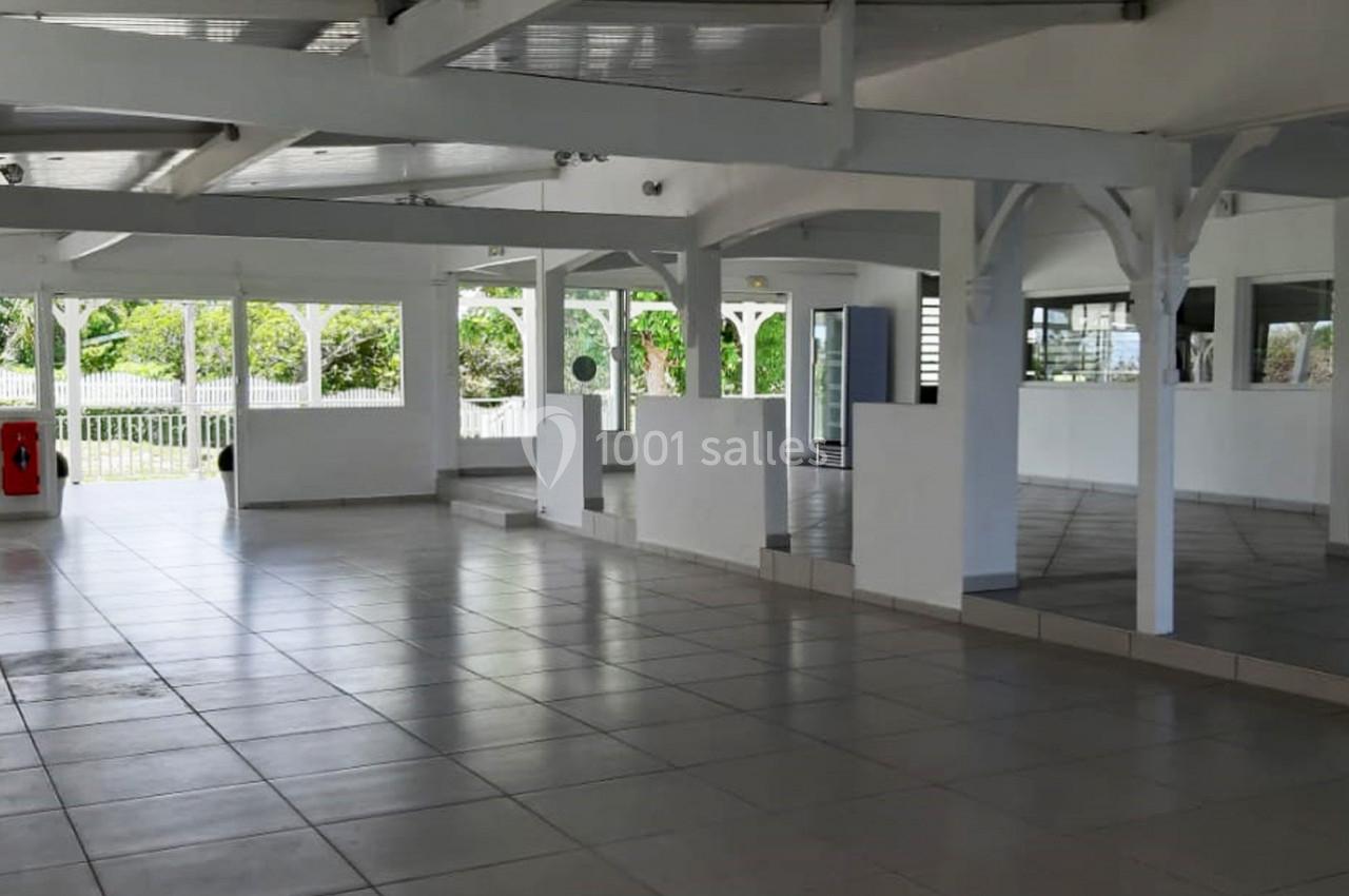 Salle spacieuse et lumineuse avec sol carrelé, grandes fenêtres et structure en bois peint en blanc.