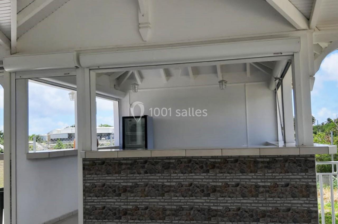 Abri extérieur avec comptoir en pierre, réfrigérateur visible à l'intérieur et structure en bois blanc.