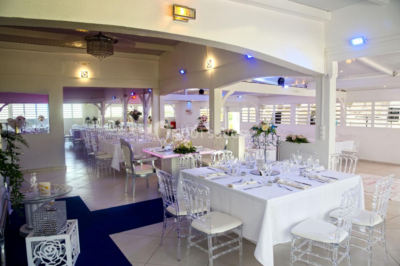 Salle de réception lumineuse avec tables décorées, chaises transparentes et arrangements floraux.